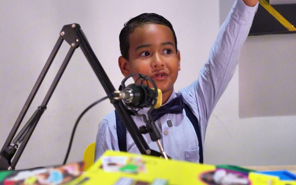 Gabo, uno de los niños de LIRA, levanta la mano mientras presenta el noticiero del programa